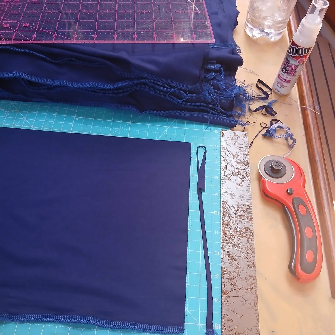 A folded length of navy fabric squared up on a cutting mat with a rotary cutter and steel rule beside it