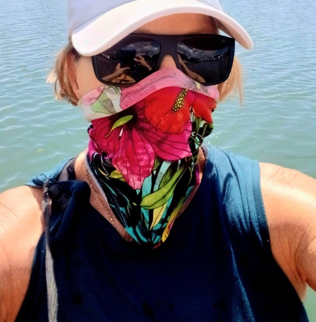 Charlotte on the boat with a bright floral neck sock pulled up over her nose and mouth against the glare